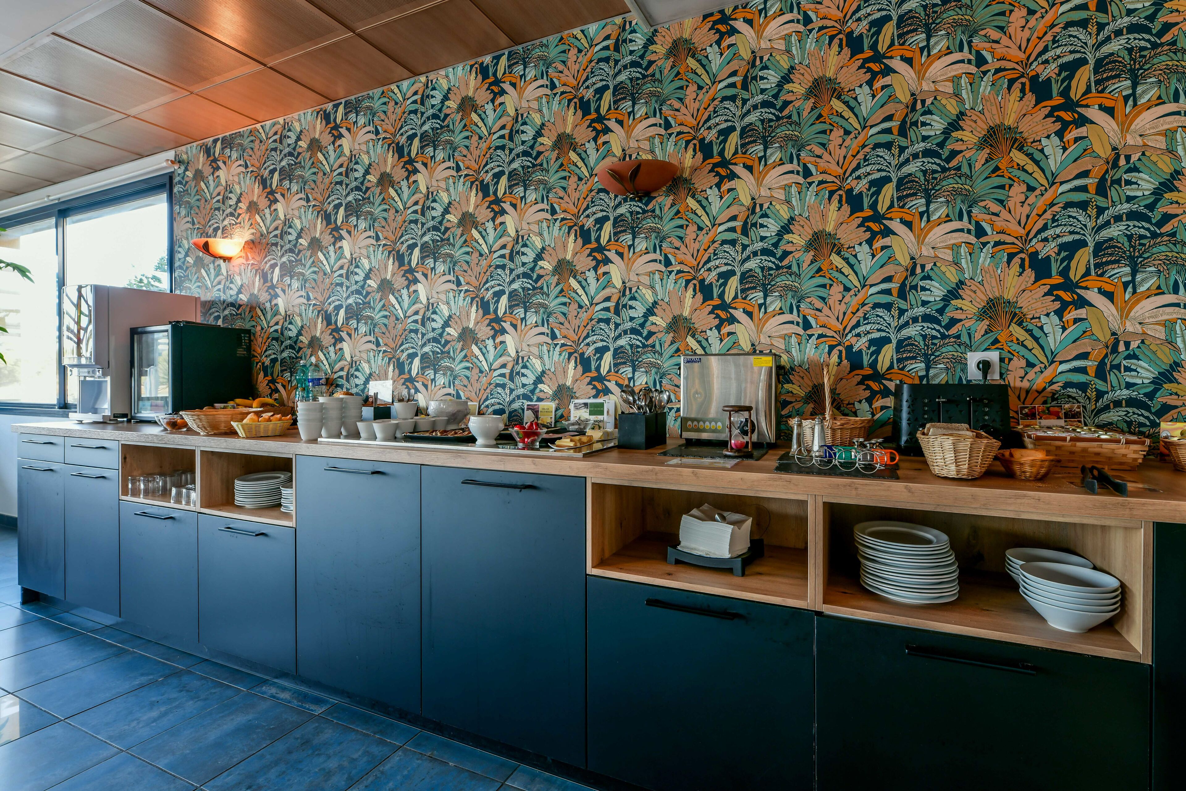 Een moderne keuken met behang met een patroon, houten kastjes en een aanrecht met diverse spullen.
