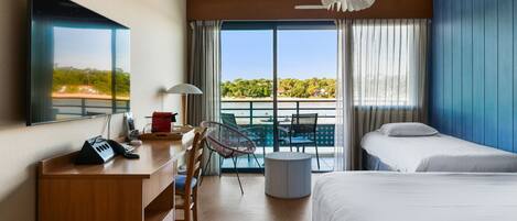 A hotel room with a desk, two beds, a balcony with a view, and a ceiling fan.