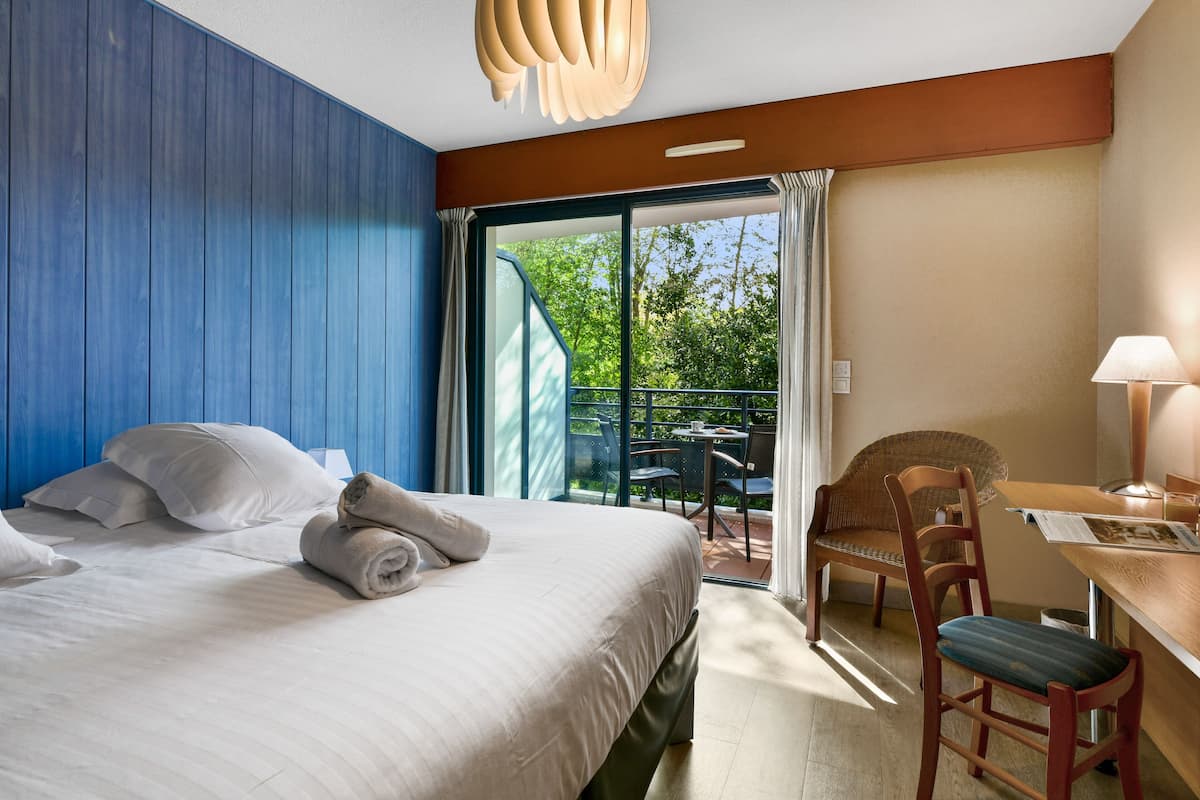 A hotel room with a bed, a desk, a chair, and a view of the outdoors.