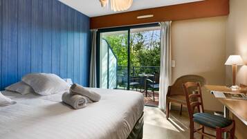A hotel room with a bed, a desk, a chair, and a view of the outdoors.
