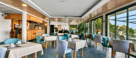 A modern restaurant with tables and chairs, a bar area, and large windows offering a view.