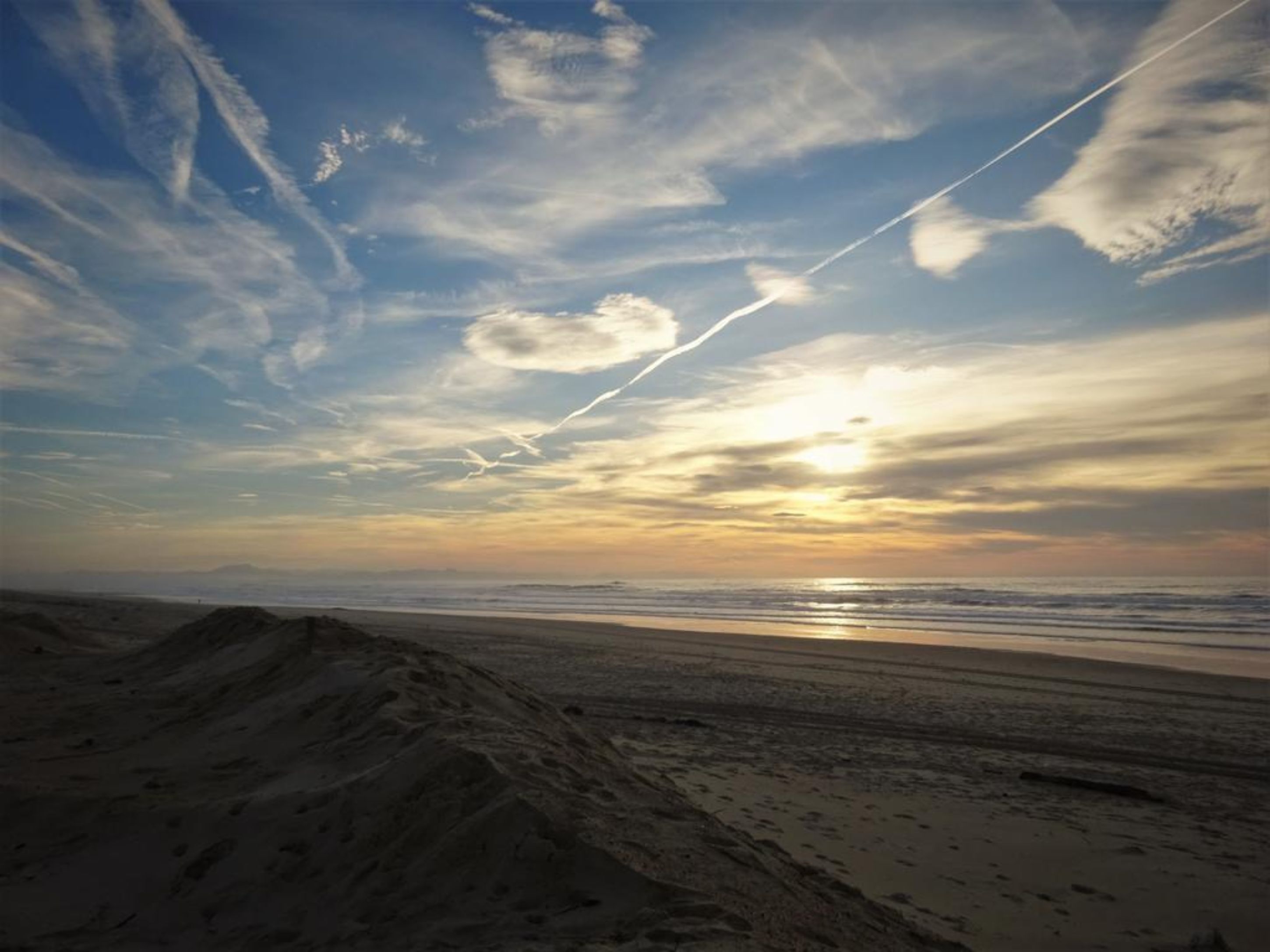 A beach with a clear sky and a visible contrail.
