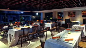 A restaurant with multiple tables set for dining, featuring a modern ceiling design and indoor plants. - HARRIS Hotel Seminyak Bali (Seminyak)