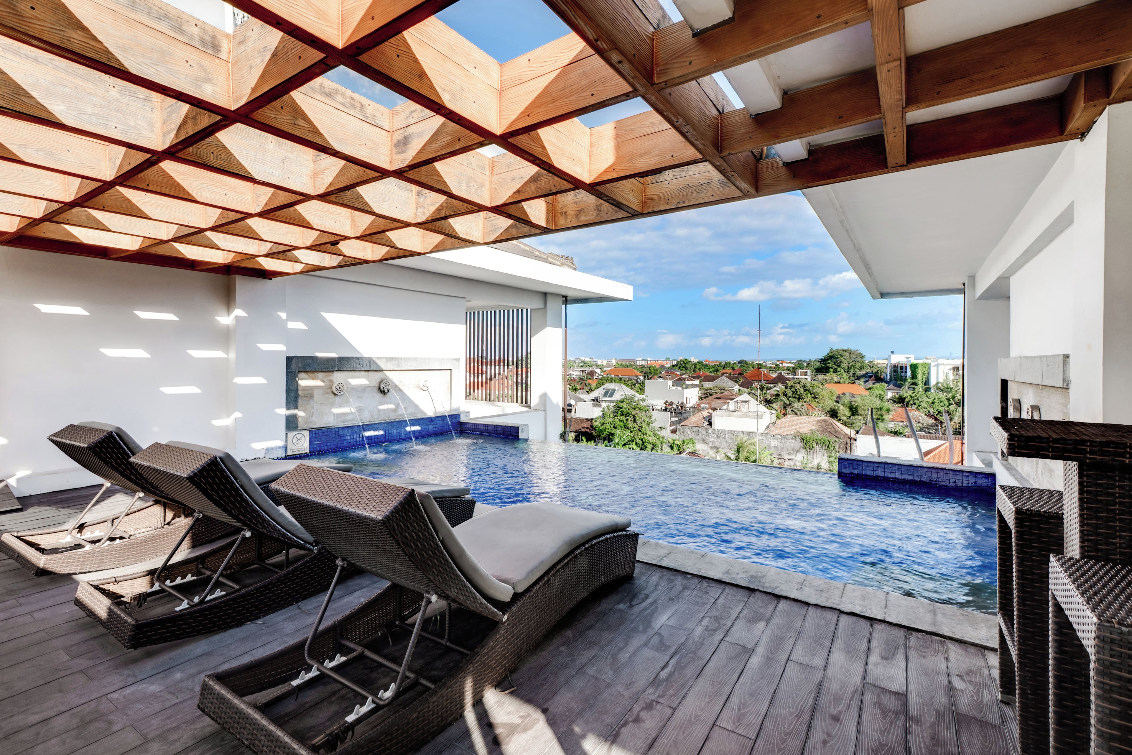 A rooftop infinity pool with lounge chairs and a view of the city.