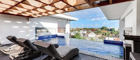 Una piscina infinita en la azotea con sillas de descanso y vistas a la ciudad.