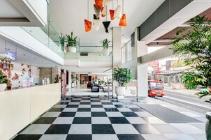 Um saguão de hotel com piso quadriculado, guarda-corpos de vidro e plantas em vasos.