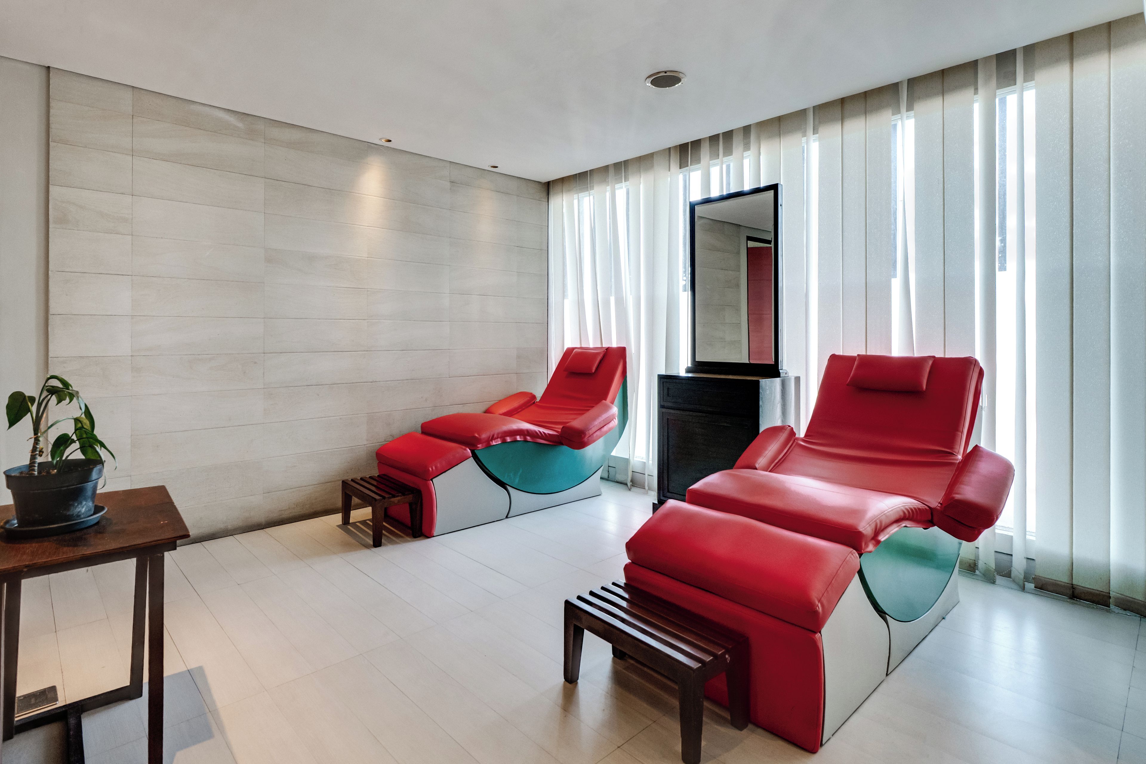 Una habitación moderna con dos sillones rojos, una mesita con una planta en maceta y un espejo grande en la pared.