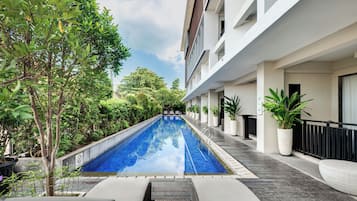 Una piscina con bordo piastrellato, circondata da piante in vaso e alberi, con un edificio su un lato.
