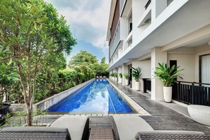 Une piscine dotée d’une terrasse carrelée, entourée de plantes en pot et d’arbres, avec un bâtiment situé sur l’un des côtés.
