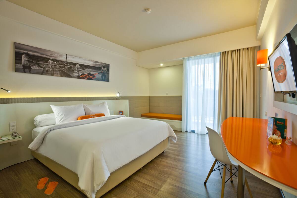 A hotel room with a large bed, a desk with a chair, a bench, and a television.