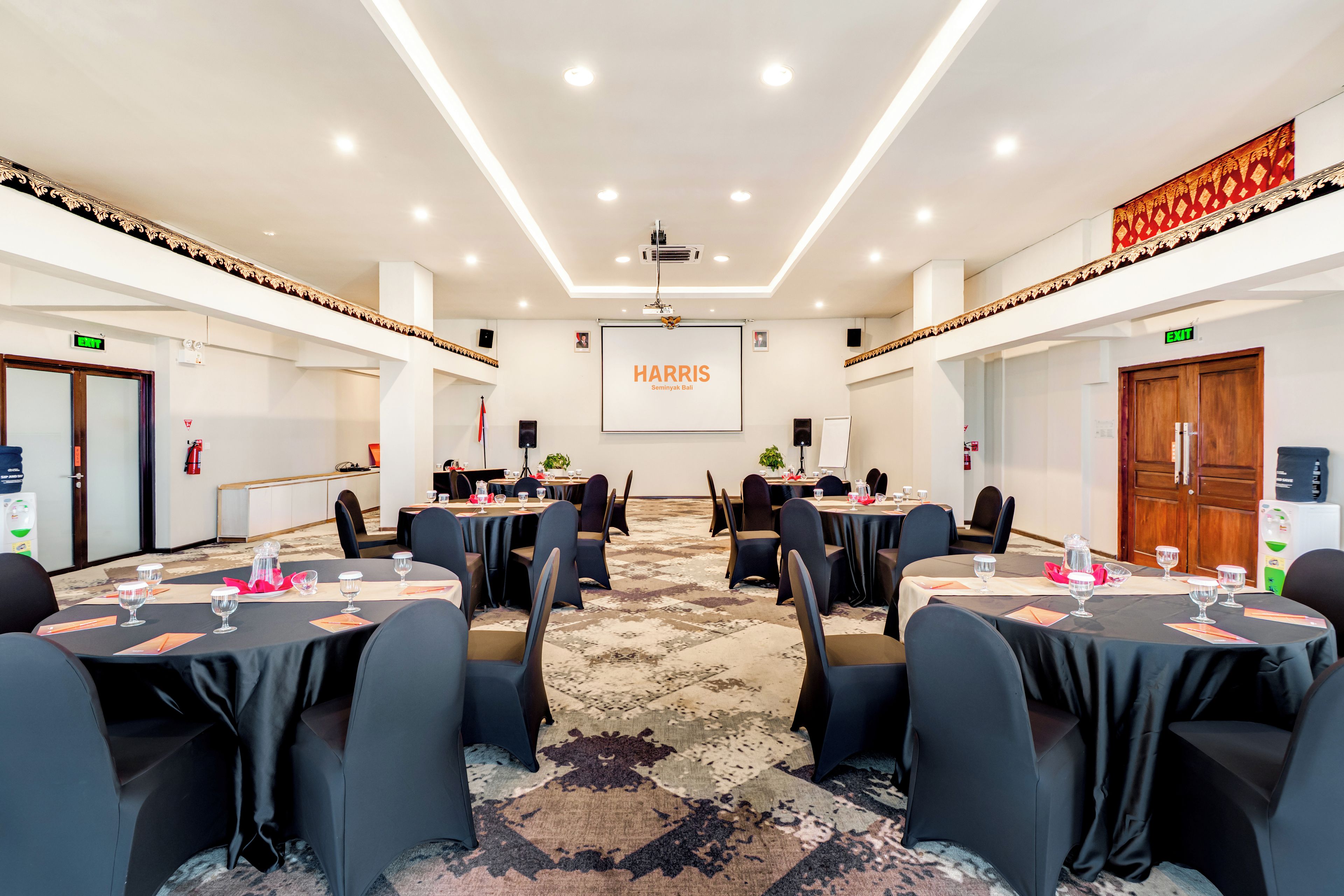 A conference room with round tables, chairs, and a projector screen displaying 'HARRIS Seminyak Bali'.