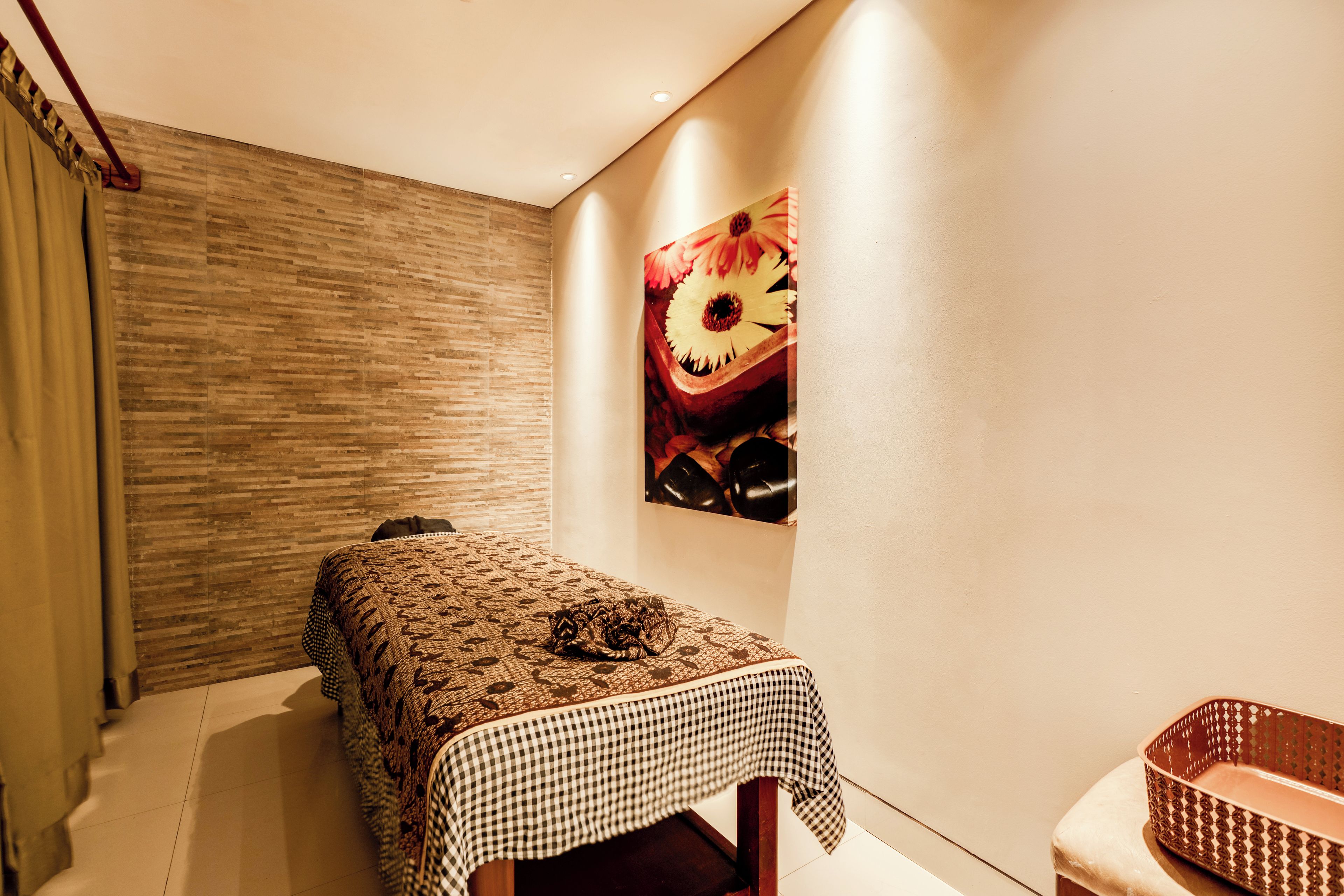 Une pièce avec un lit recouvert d ’une literie à motifs, une nappe à carreaux, une œuvre d’art accrochée au mur et une chaise en osier.