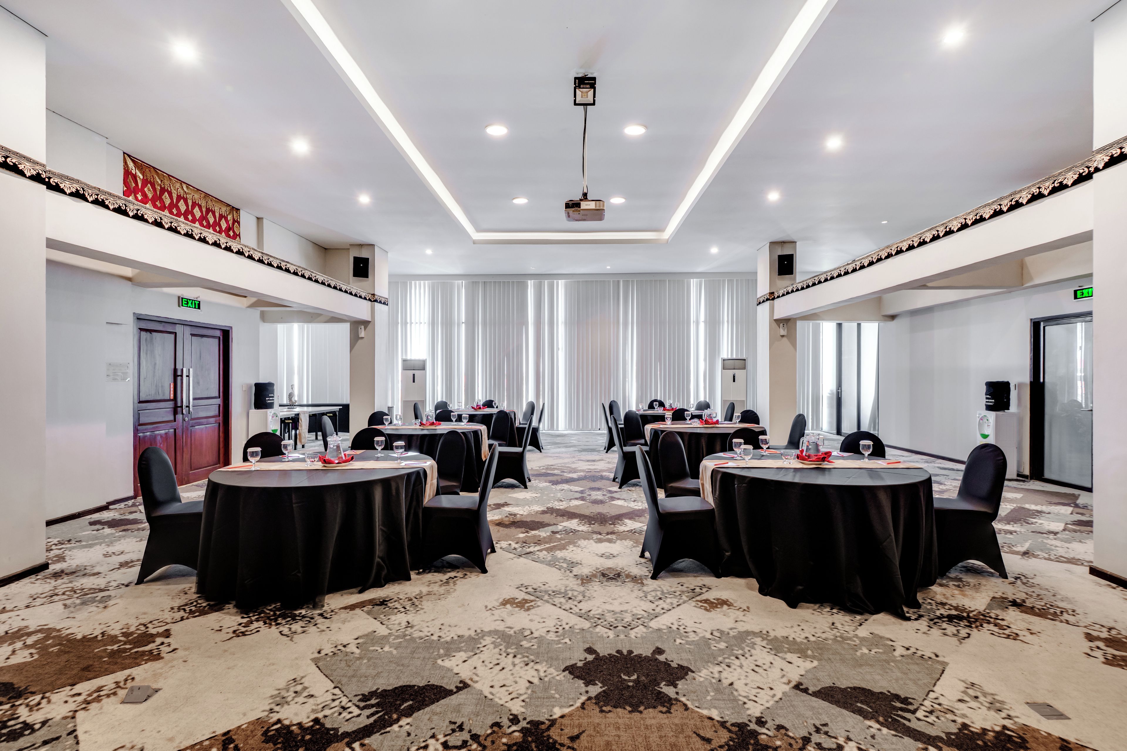 Una sala conferenze con tavoli rotondi, sedie nere e una moquette fantasia.