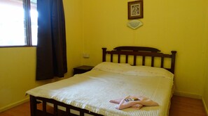 A bedroom with a bed, a nightstand, a window with curtains, and a wall-mounted fan.