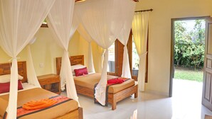 Habitación con dos camas, cada una con dosel, y vista a un jardín a través de una puerta abierta.