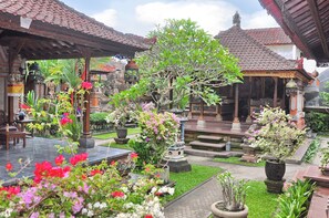A traditional courtyard with stone benches, potted plants, and a central tree. - Nick's Homestay (Ubud)
