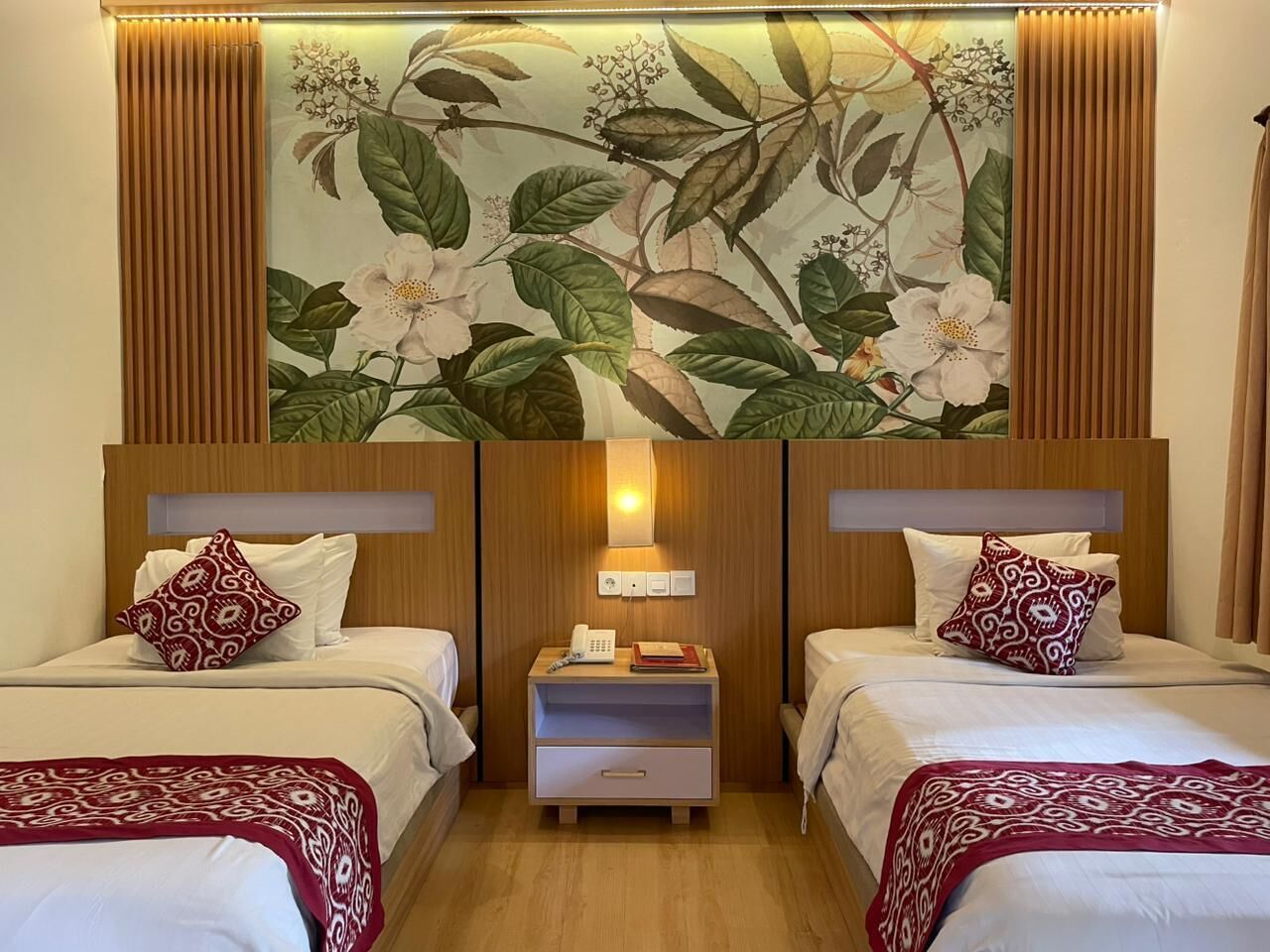 A hotel room with two beds, a nightstand with a lamp, and a floral wall mural.