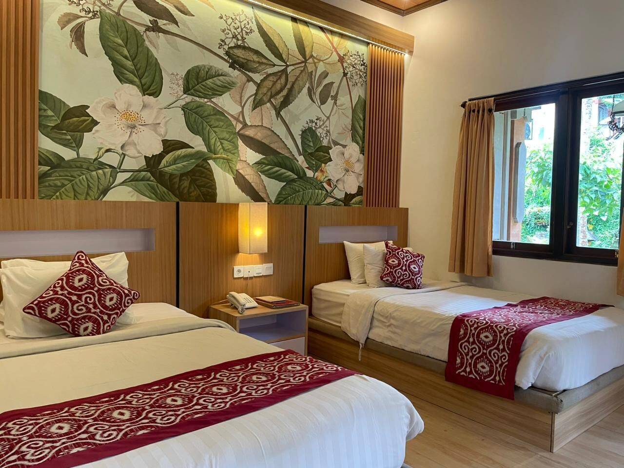 A hotel room with two beds, a large floral wall mural, a wooden headboard, and a window with curtains.