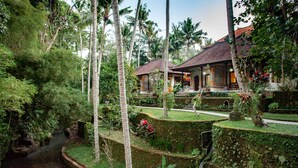 A tropical resort with a water channel, lush greenery, and traditional-style buildings with tiled roofs. - Nick's Pension (Ubud)