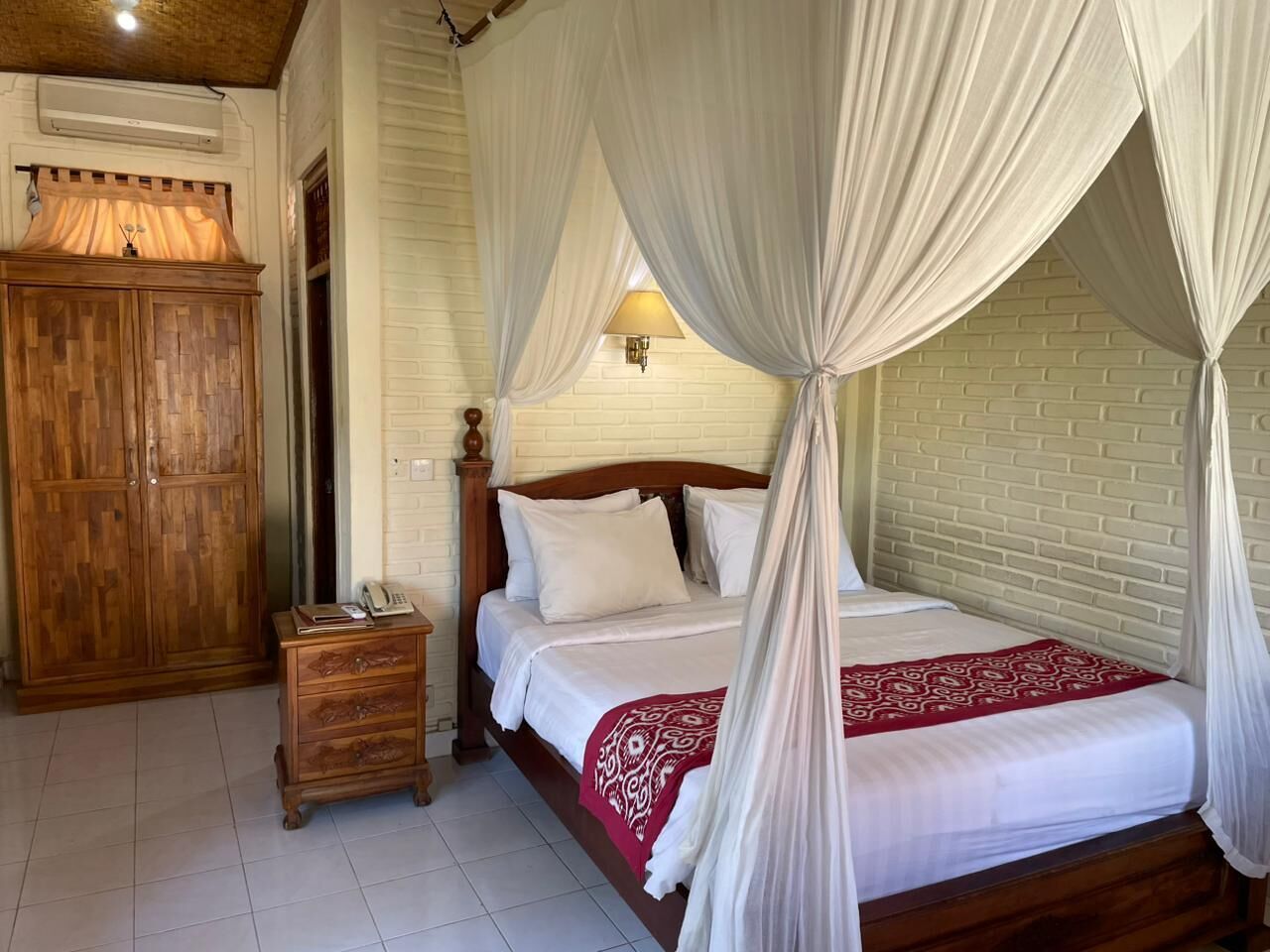 A bedroom with a four-poster bed, wooden wardrobe, bedside table, and a lamp.
