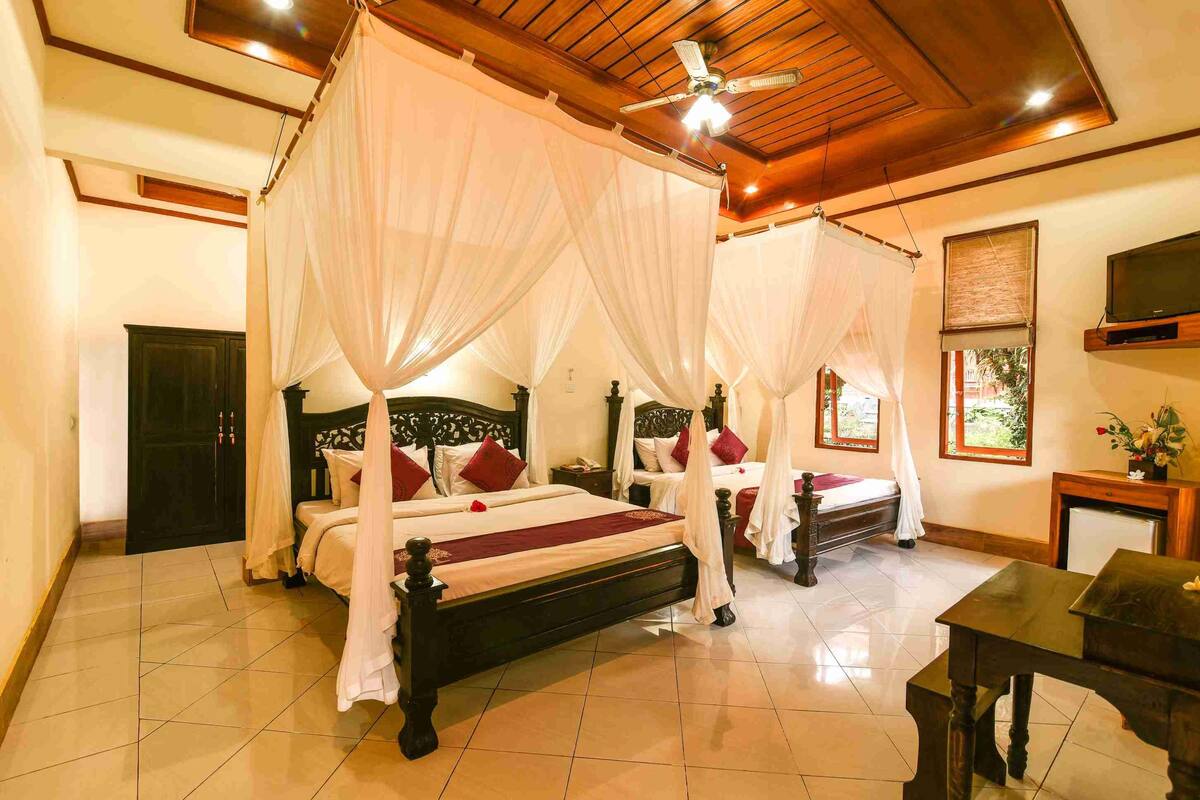 A four-poster bed with white canopy, a wooden ceiling, and a television on the wall.