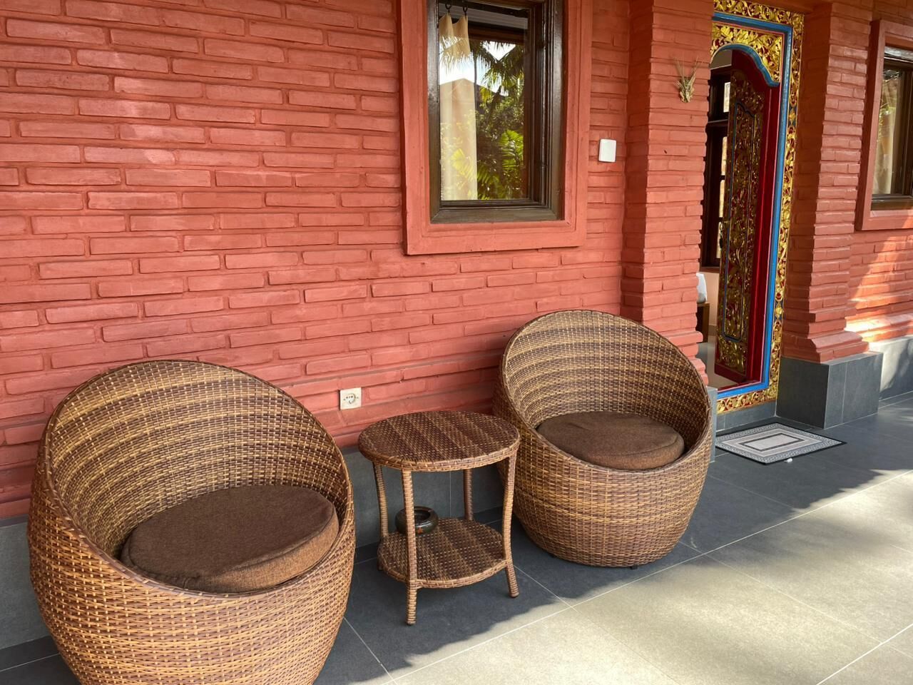 Wicker furniture near a red brick building with a window and a decorative door.