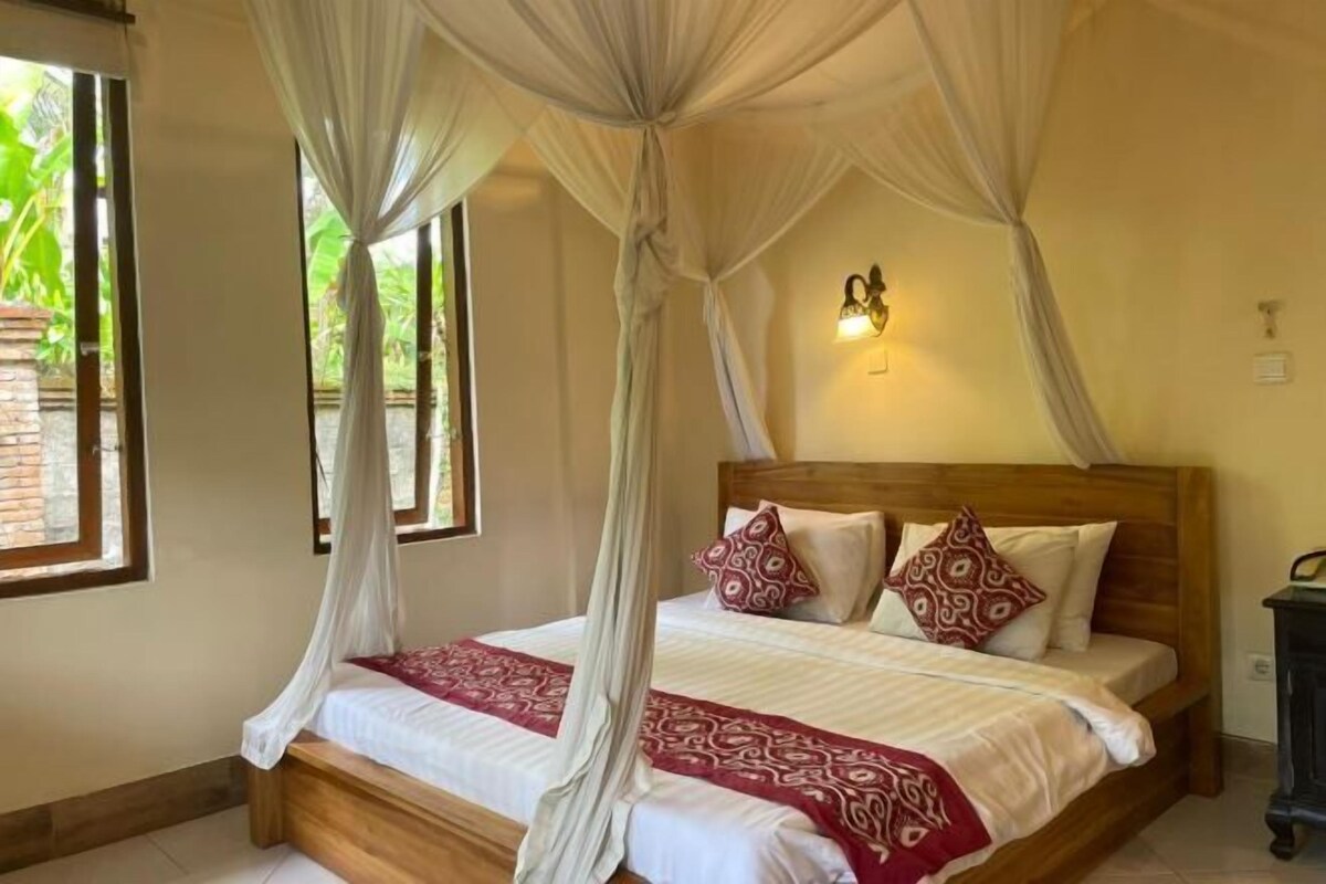 A four-poster canopy bed with a wooden headboard, two bedside tables, and a wall-mounted light fixture.