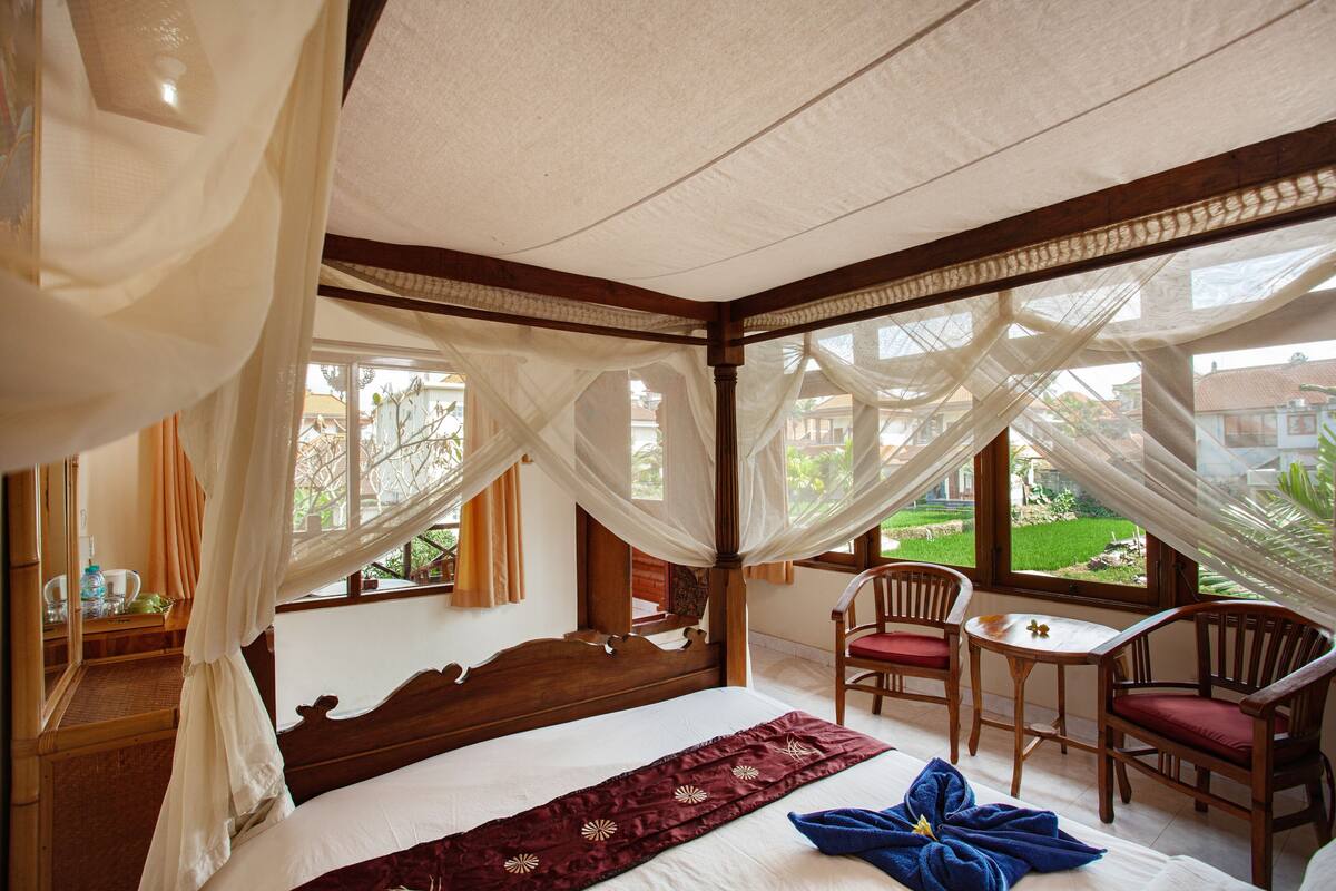A bedroom with a bed, a wooden chair, a small table, and a view of the outside.