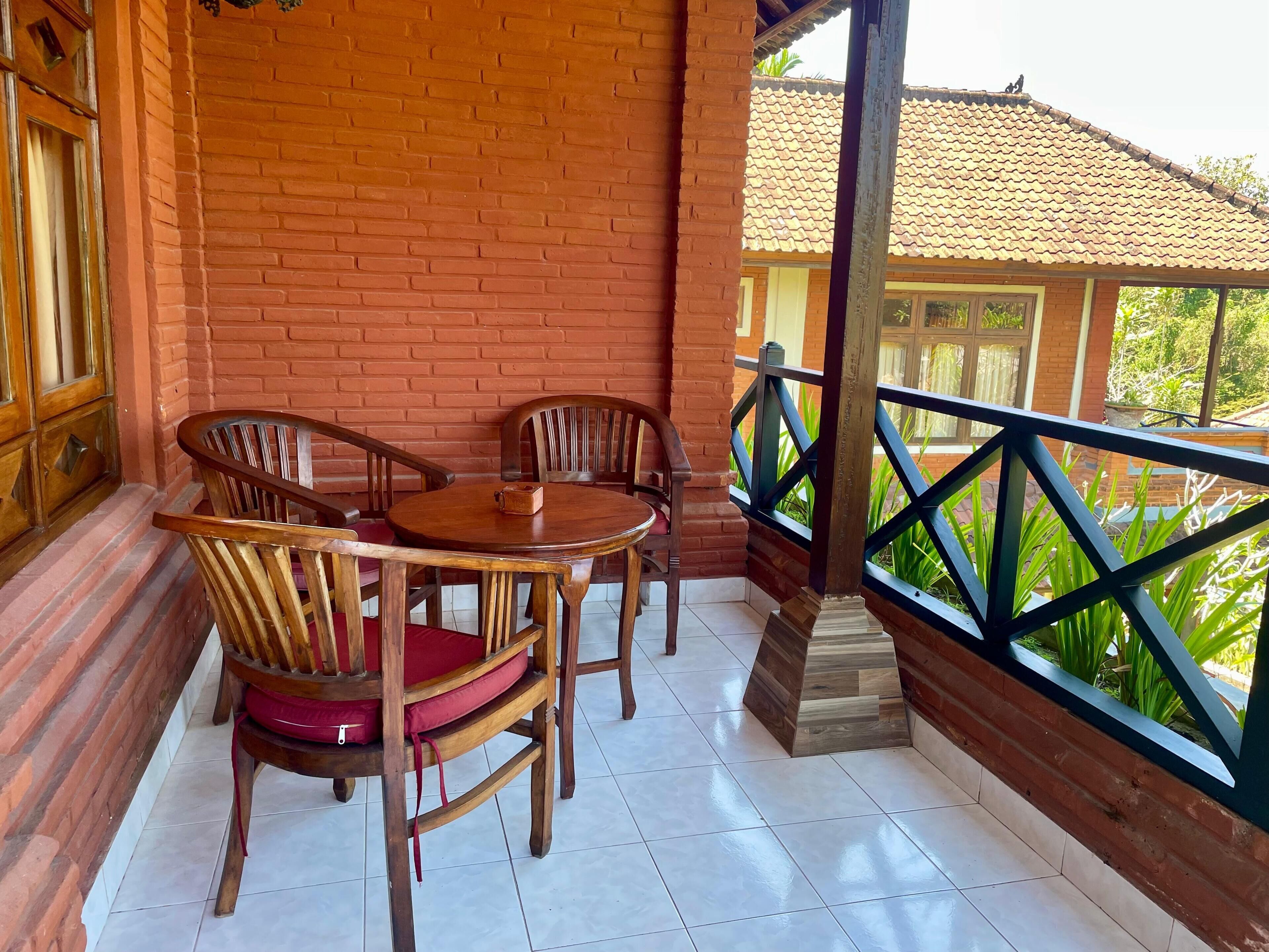A covered outdoor seating area with brick walls, wooden furniture, and a view of a building with a tiled roof.