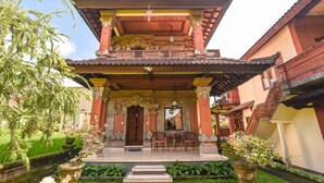 A traditional building with a multi-tiered roof, a central staircase, and a small outdoor seating area with chairs and a table. - Nick's Pension (Ubud)
