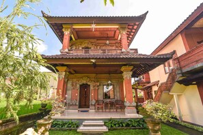 A traditional building with a multi-tiered roof, a central staircase, and a small outdoor seating area with chairs and a table. - Nick's Pension (Ubud)