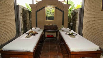 Quarto com duas camas de madeira, uma mesinha com velas e um quadro na parede.