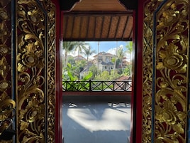 Un balcón con barandillas doradas ornamentales y vista a una zona residencial con palmeras y casas.