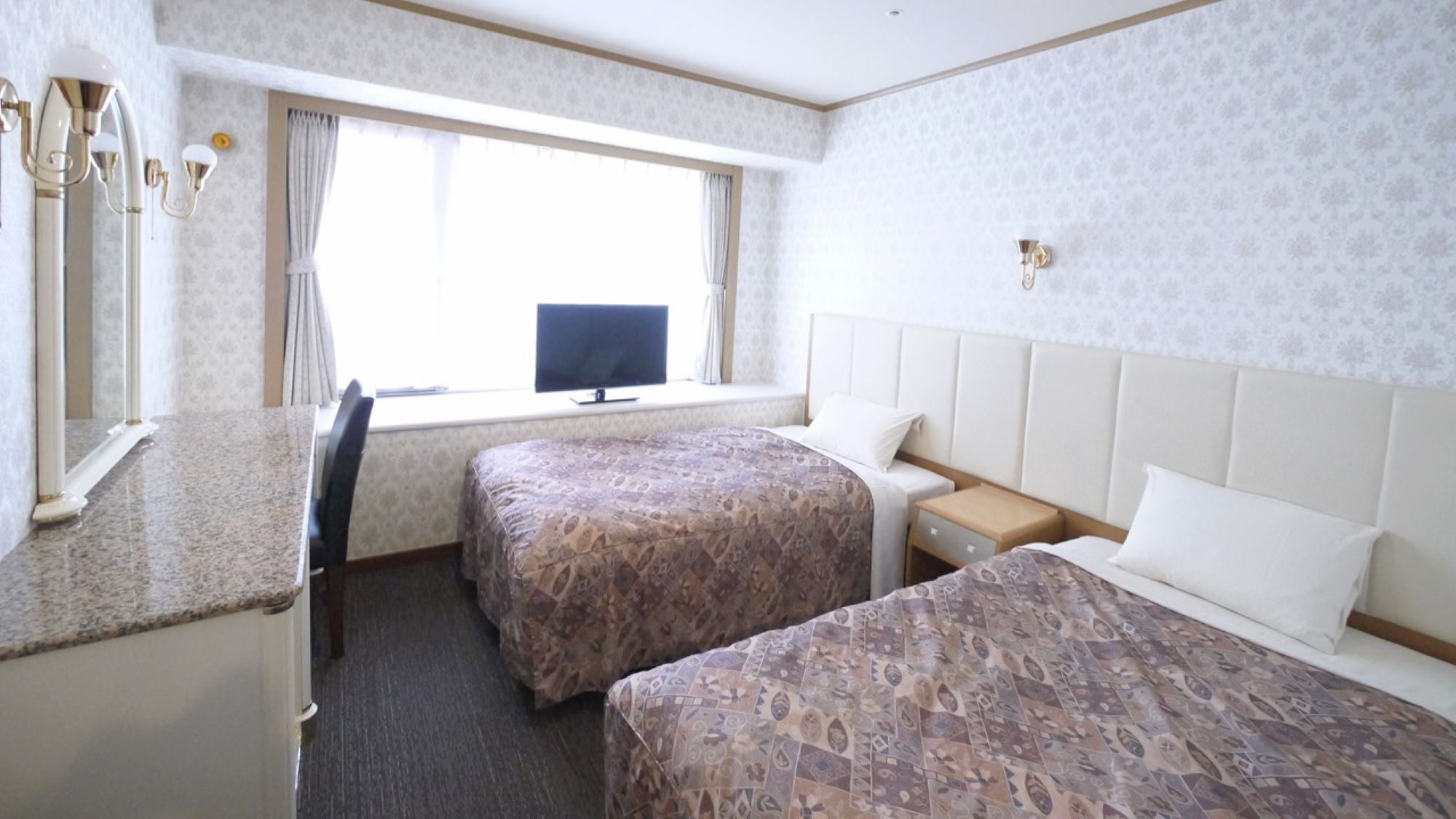 A hotel room with two beds, a desk, a television, and a window with curtains.