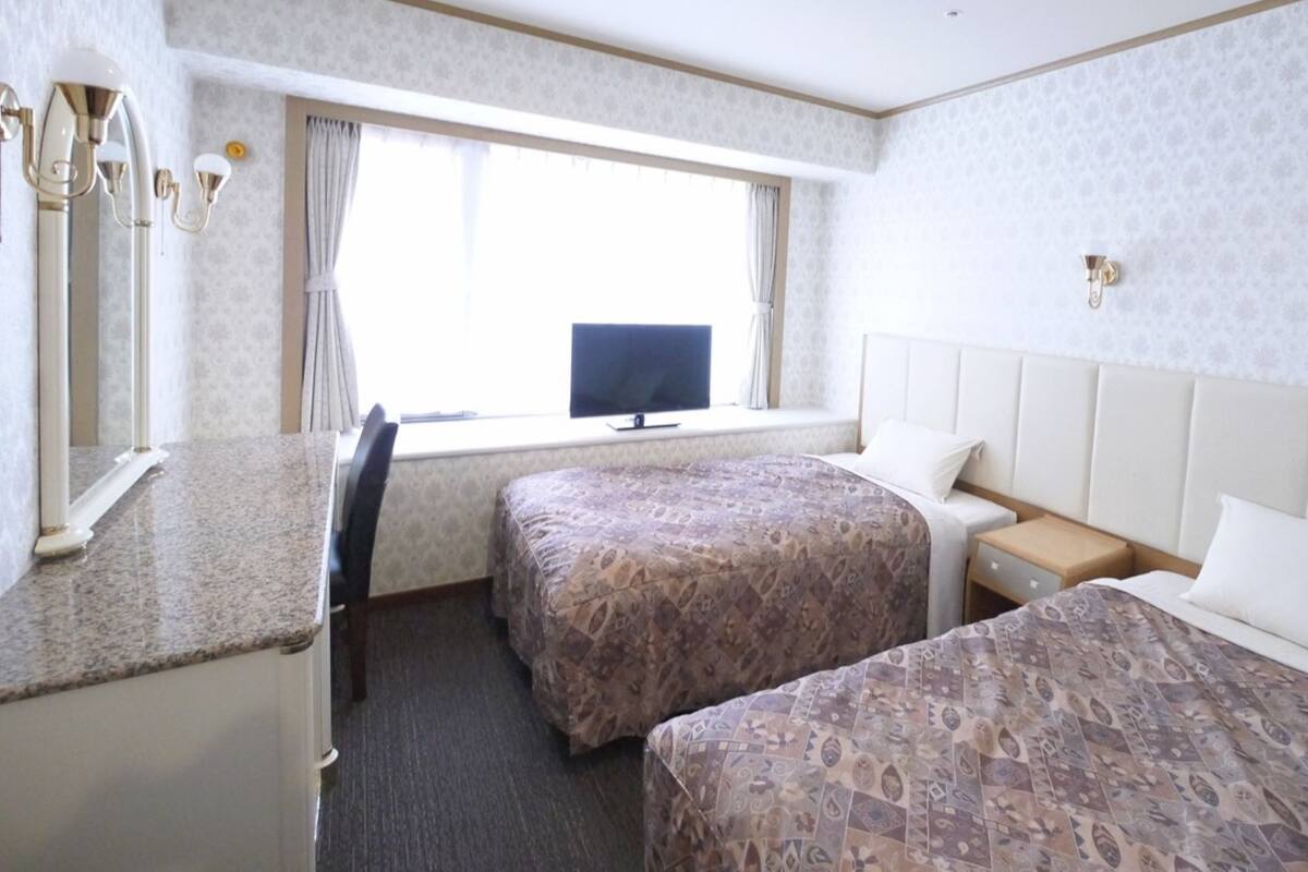 A hotel room with two beds, a desk, a television, and a window with curtains.