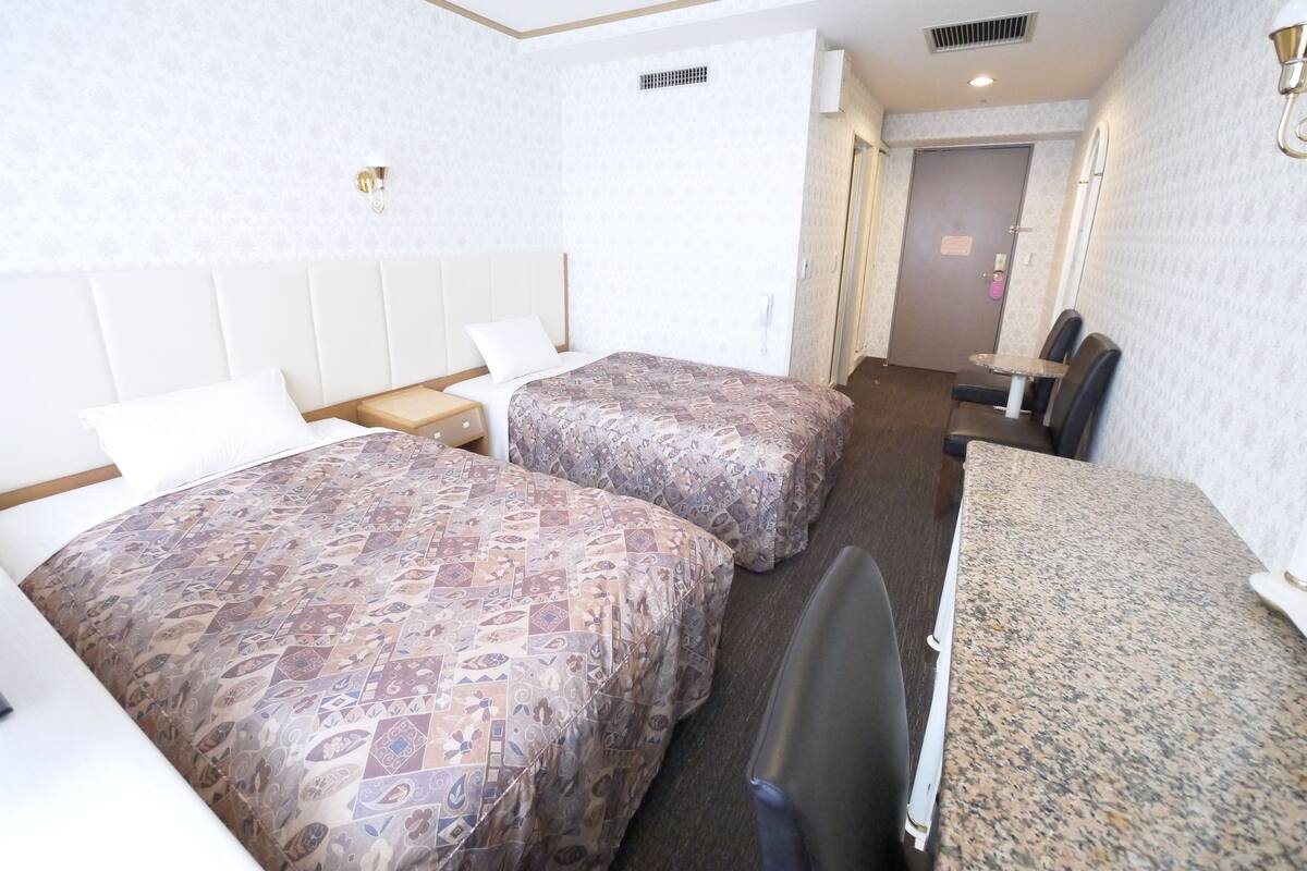 A hotel room with two beds, a desk, and a chair.