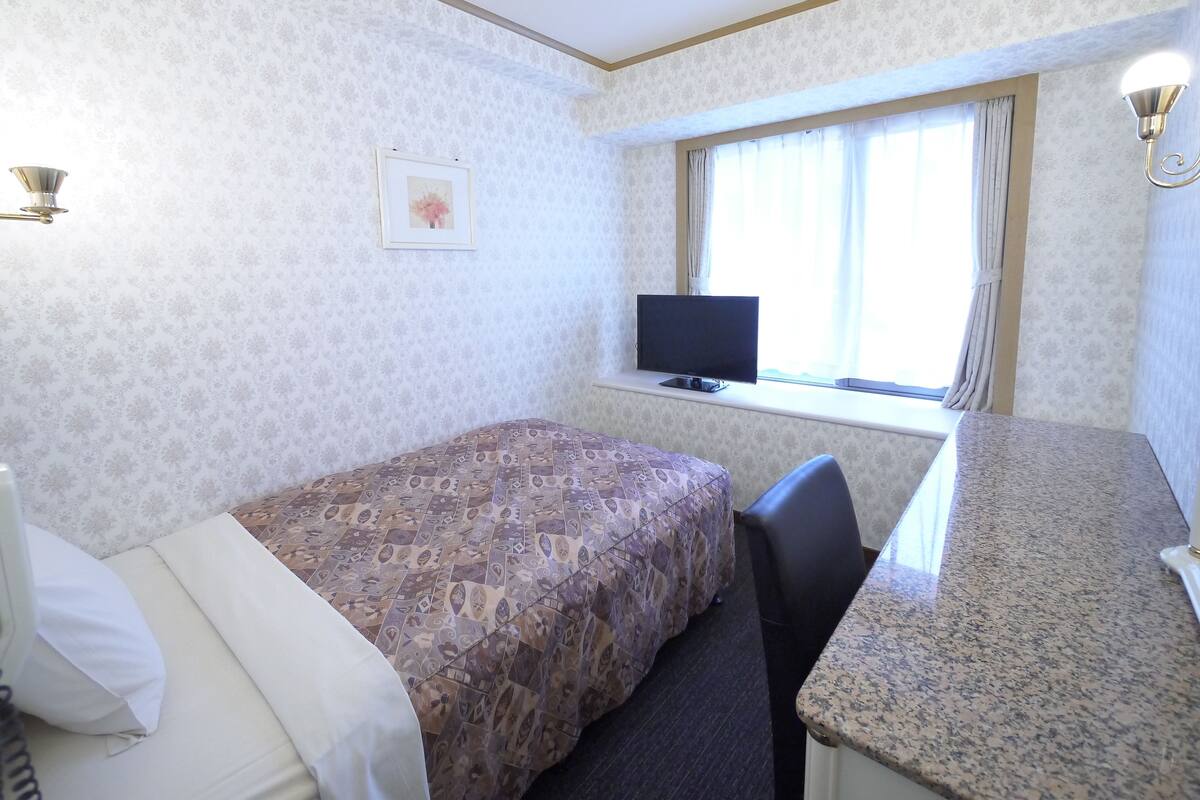 A hotel room with a bed, a desk, a chair, a television, and a window with curtains.