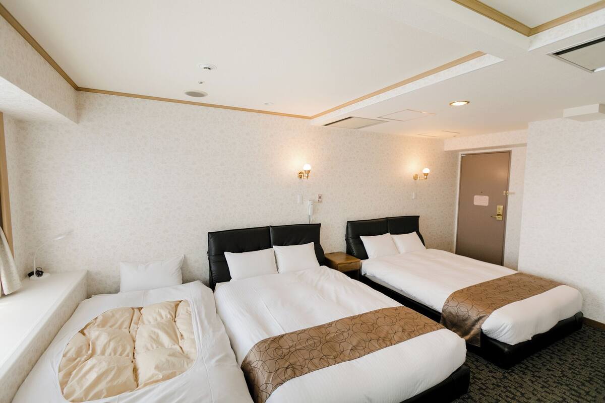 A hotel room with two beds, a window, a door, and a ceiling with recessed lighting.
