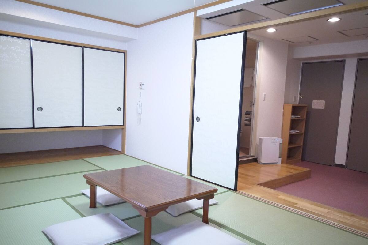 A traditional tatami mat room with a wooden table and cushions, a sliding door, and a small heater.