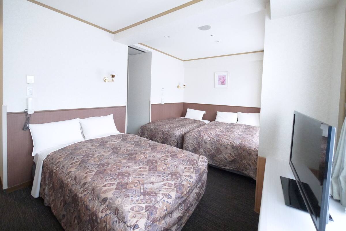 A hotel room with two beds, a TV, and a door leading to another room.