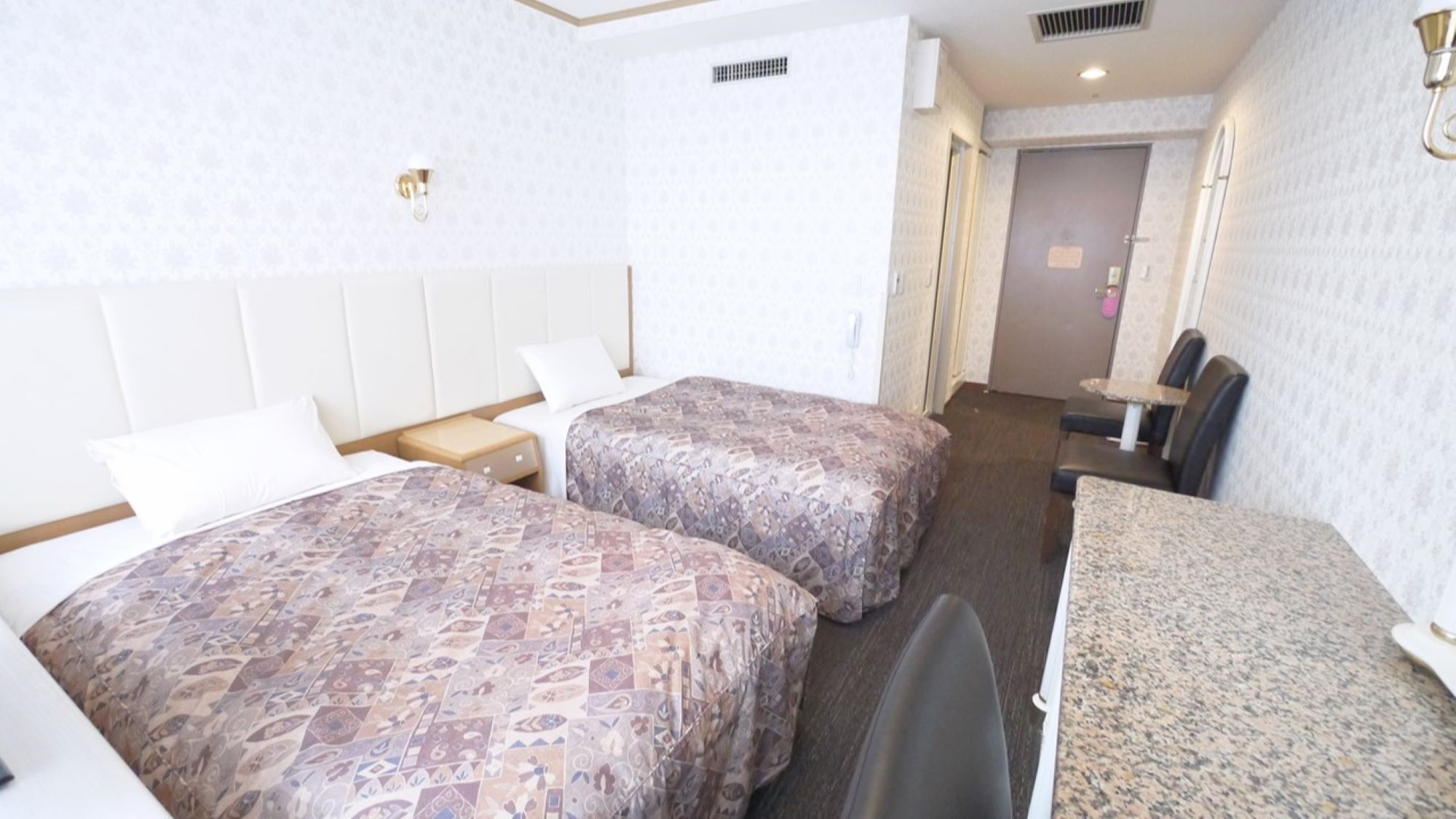 A hotel room with two beds, a desk, a chair, and a small table.