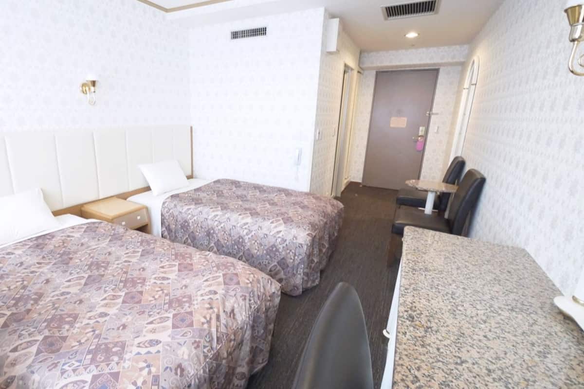 Camera d'albergo con due letti, una scrivania, una sedia e un piccolo tavolo.