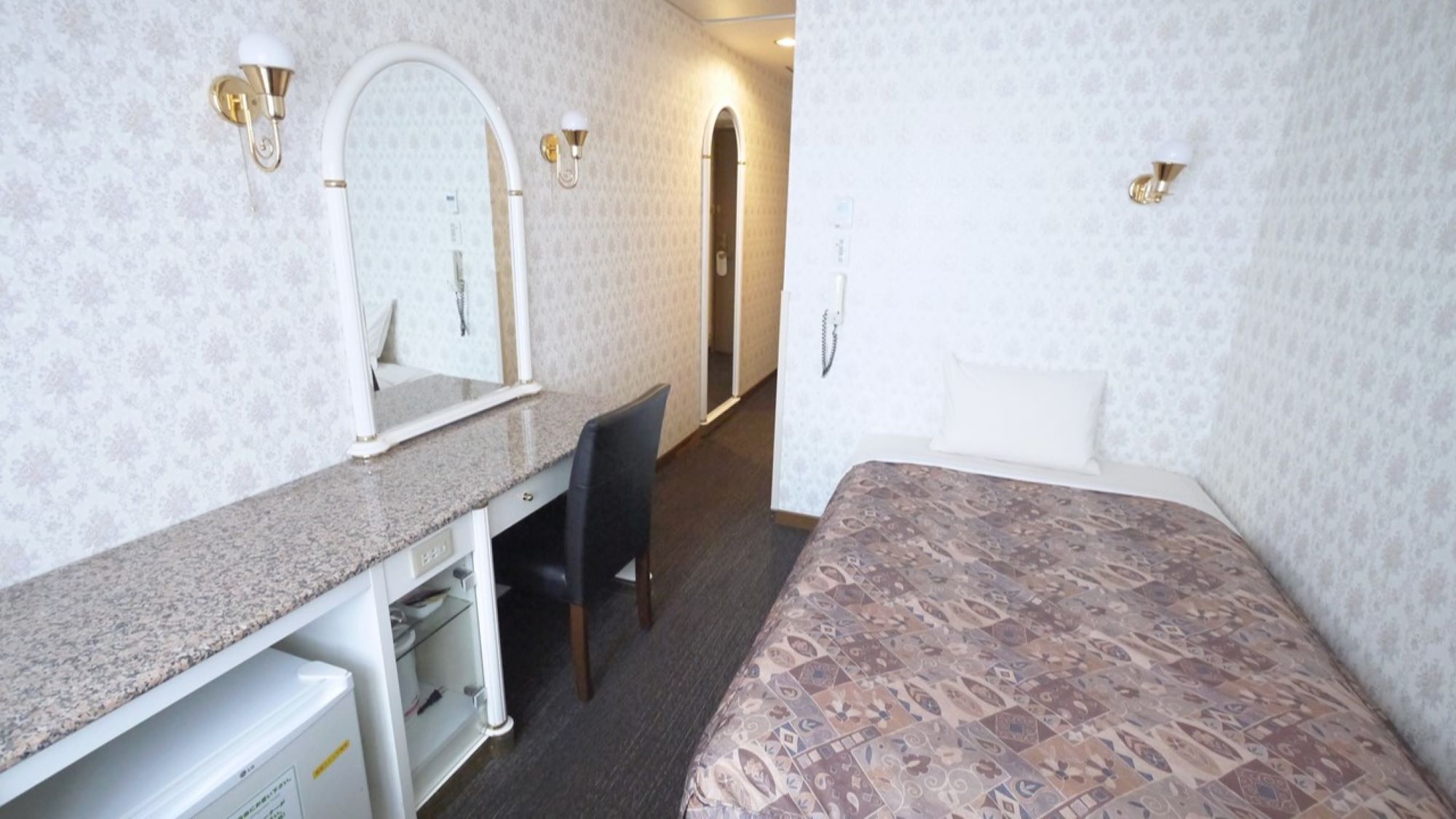 A hotel room with a bed, a desk with a chair, a mirror, and a door leading to another room.