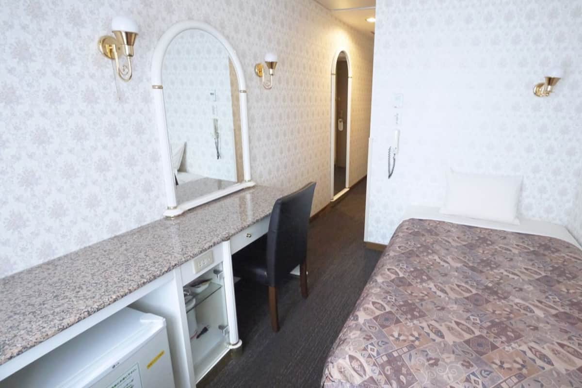 Una camera d'albergo con un letto, una scrivania con sedia, uno specchio e una porta che conduce a un'altra stanza.