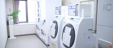 A laundry room with multiple washing machines, a window with curtains, and a sign on the wall.