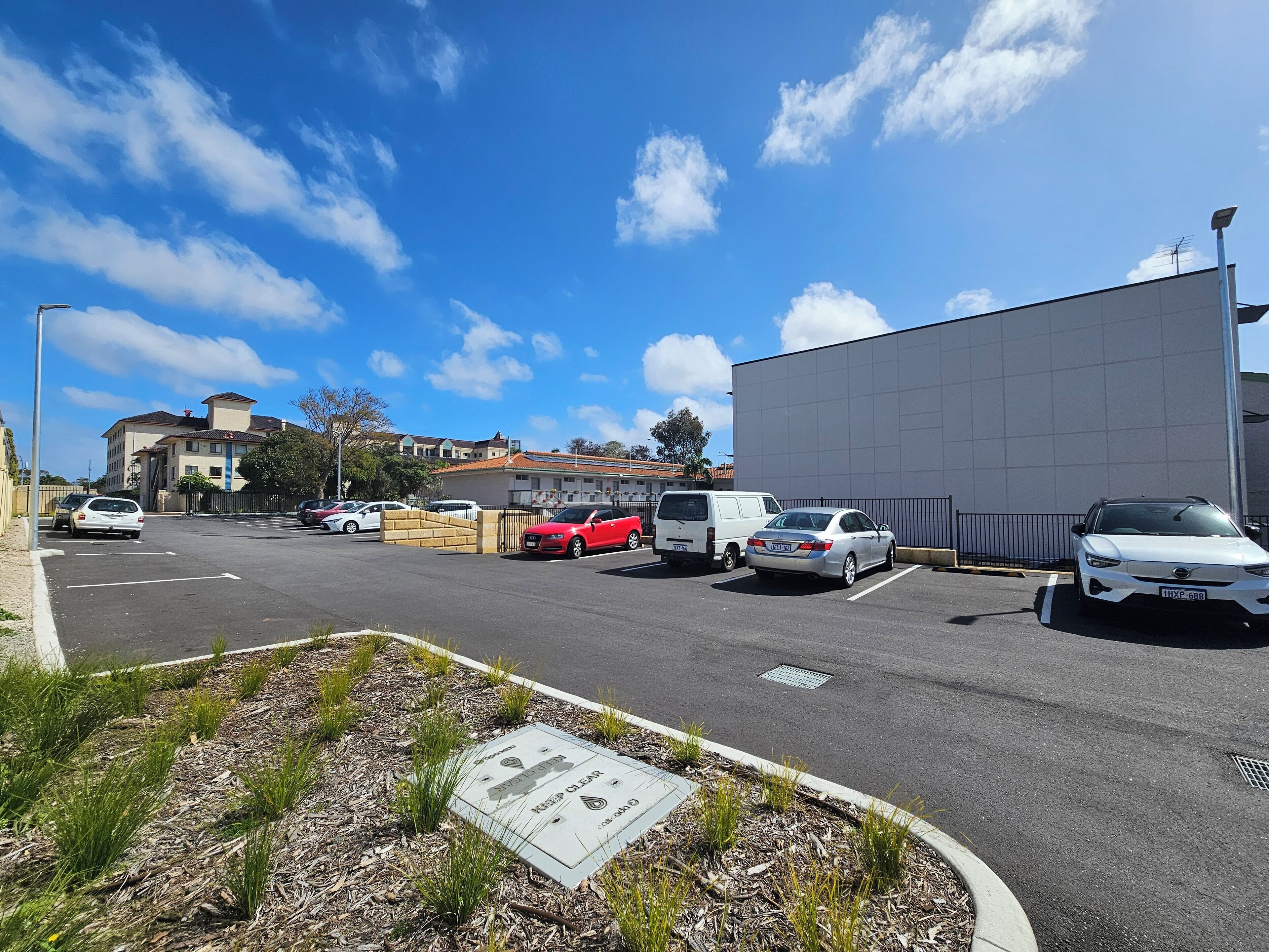 A parking lot with several cars, a large building, and a clear sky.