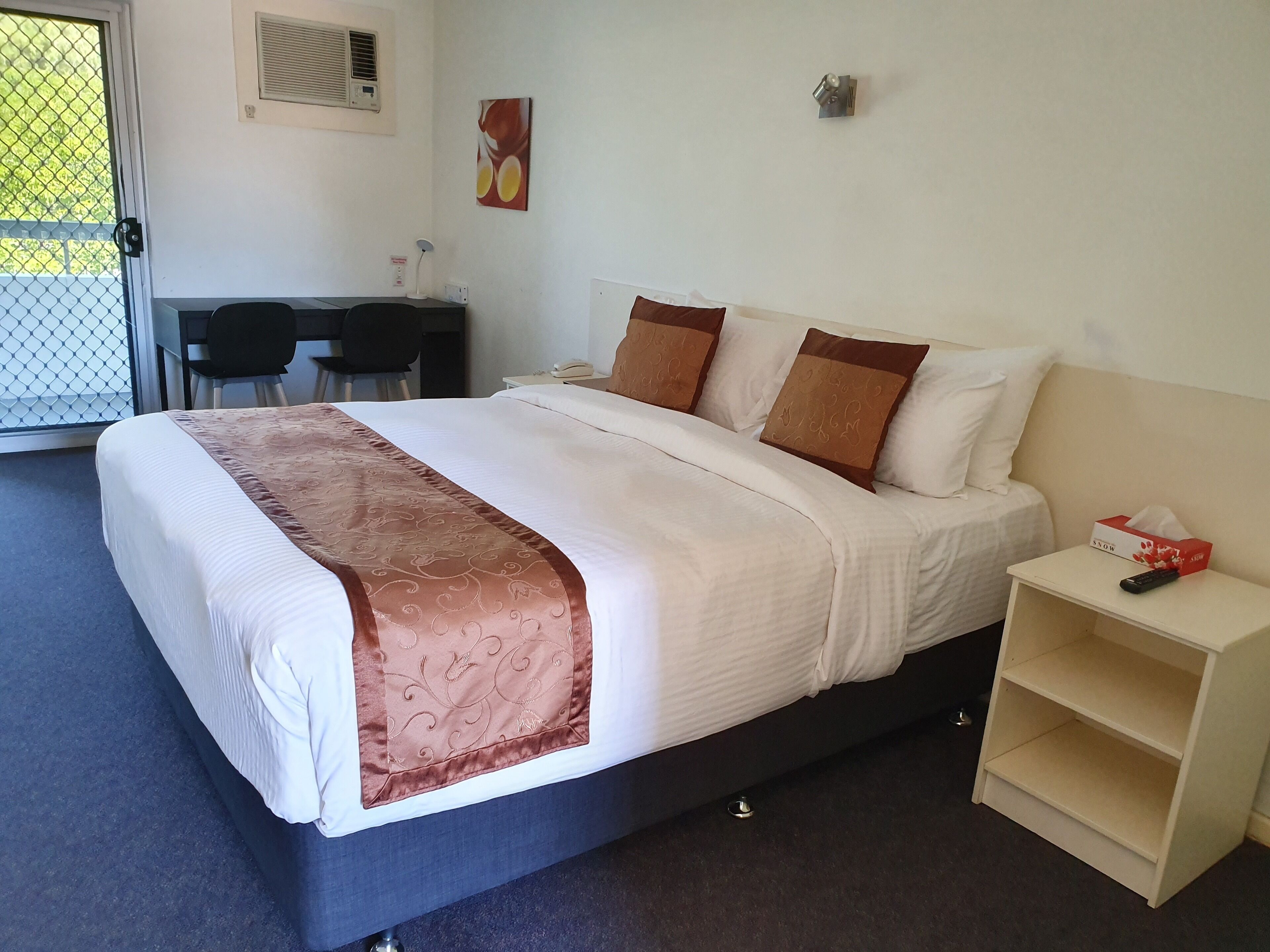 Una habitación de hotel con cama, mesita de noche y escritorio con sillas.