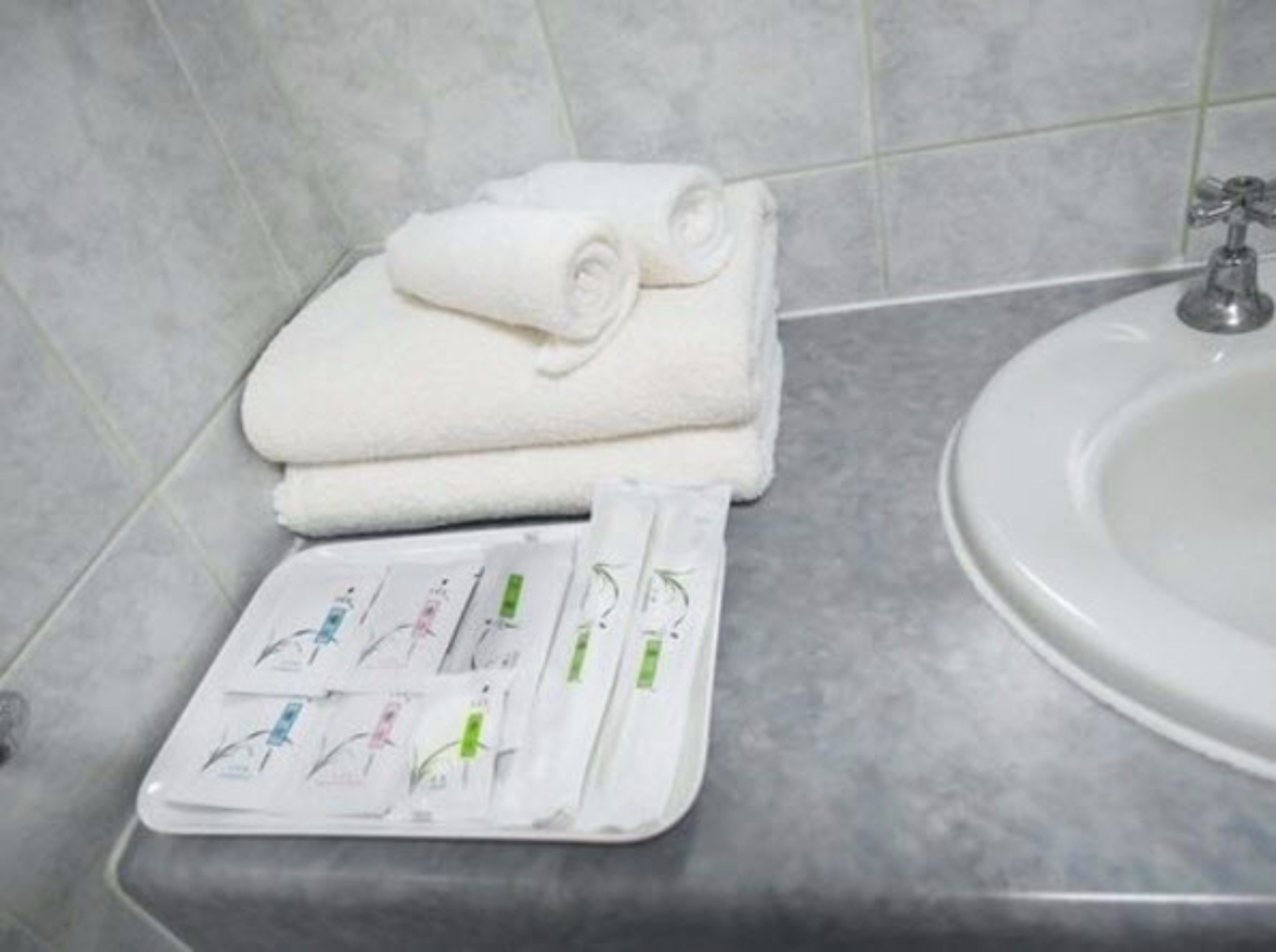 Un baño con lavamanos blanco, una toalla y un recipiente con artículos de aseo.