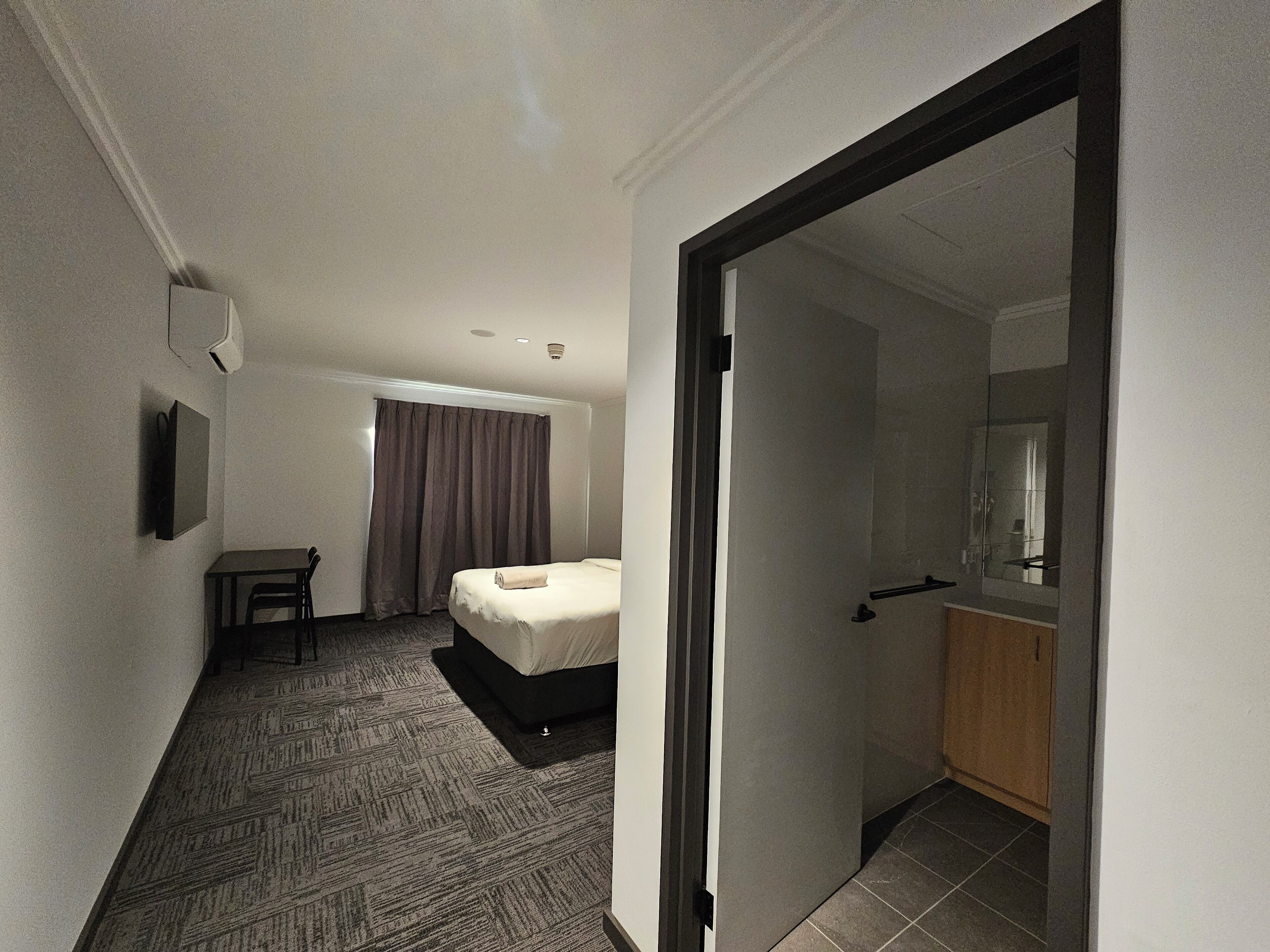 A hotel room with a bed, a desk, a chair, a television, and a bathroom visible through an open door.