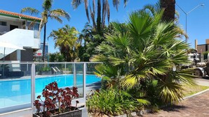A pool area with a clear view of the water, surrounded by palm trees and a building with a red roof.